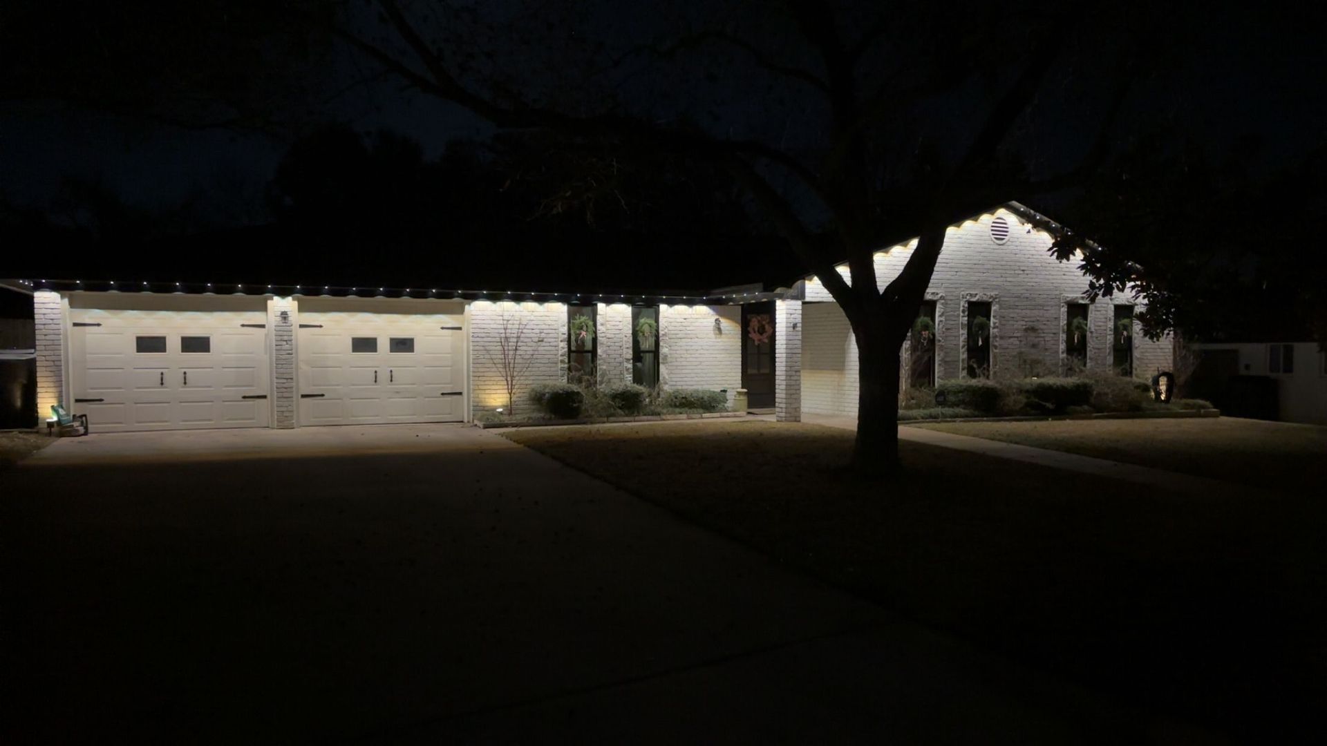 Dimly lit white building with garage doors and a tree in the foreground at night