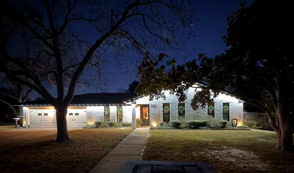 House decorated with red and green holiday lights at night, with lit windows and a front walkway.