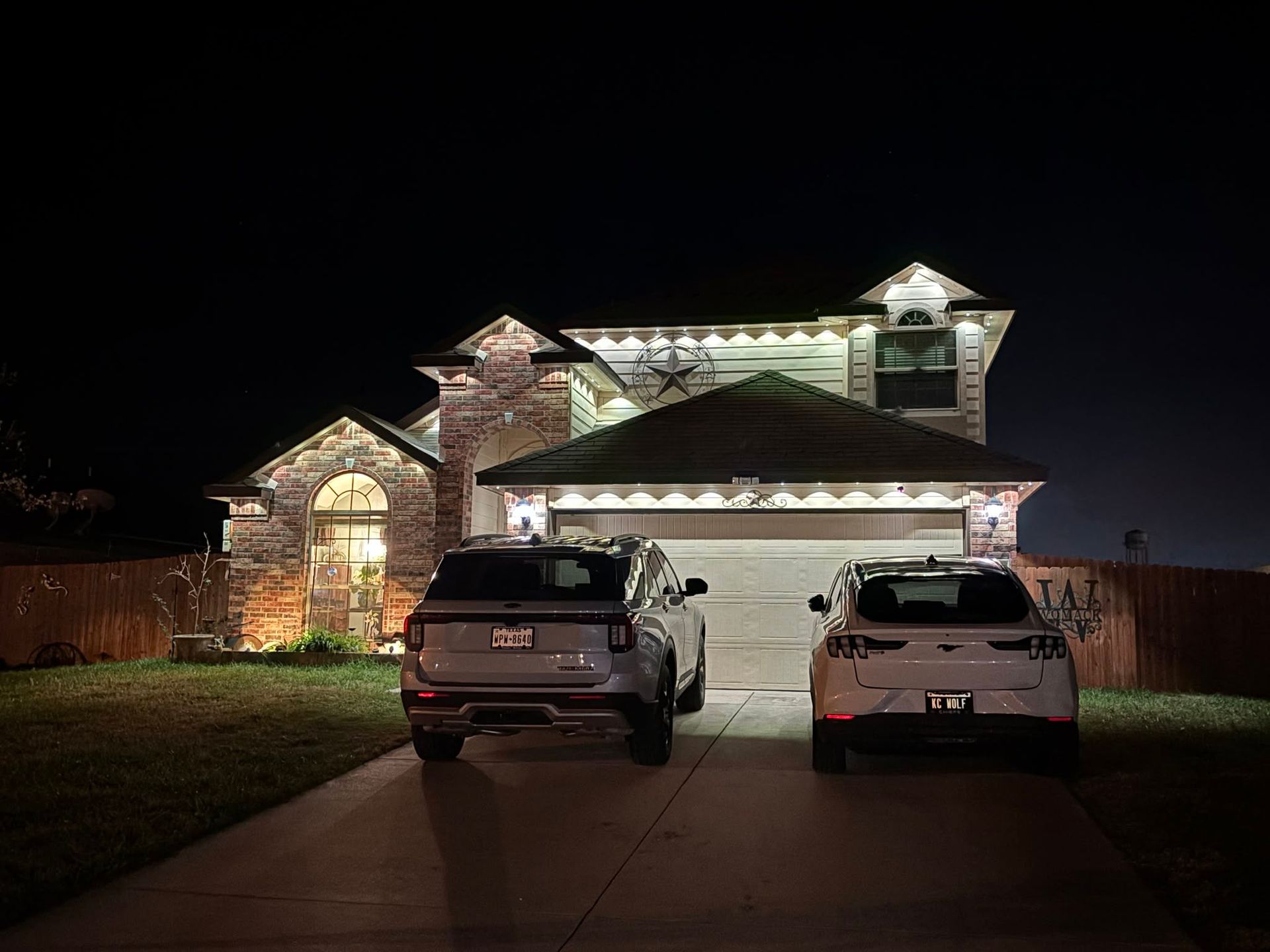 Two SUVs parked in a driveway at night in front of a lit suburban house
