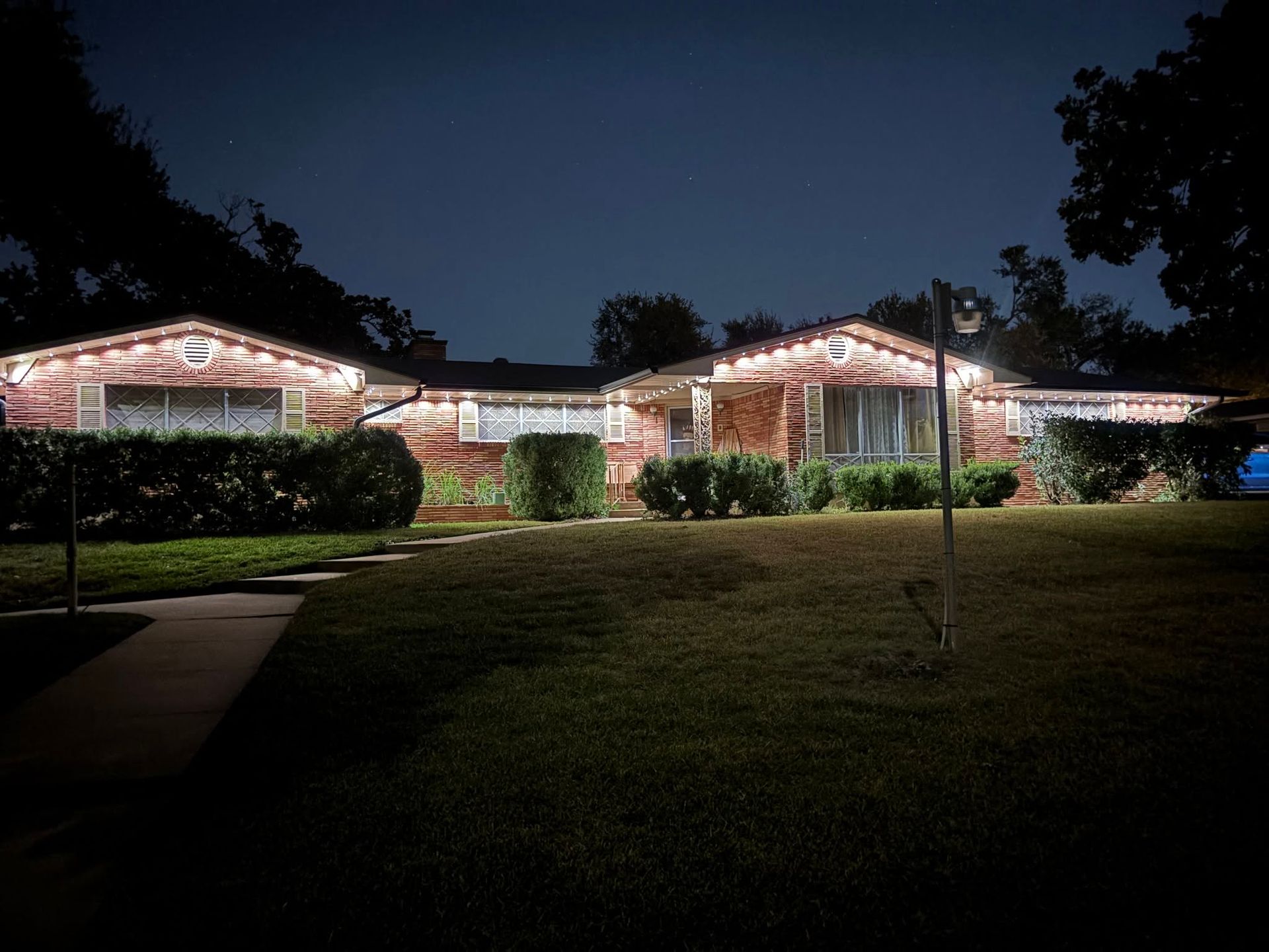 Lit house with Christmas lights at night, framed by a dark lawn and trees
