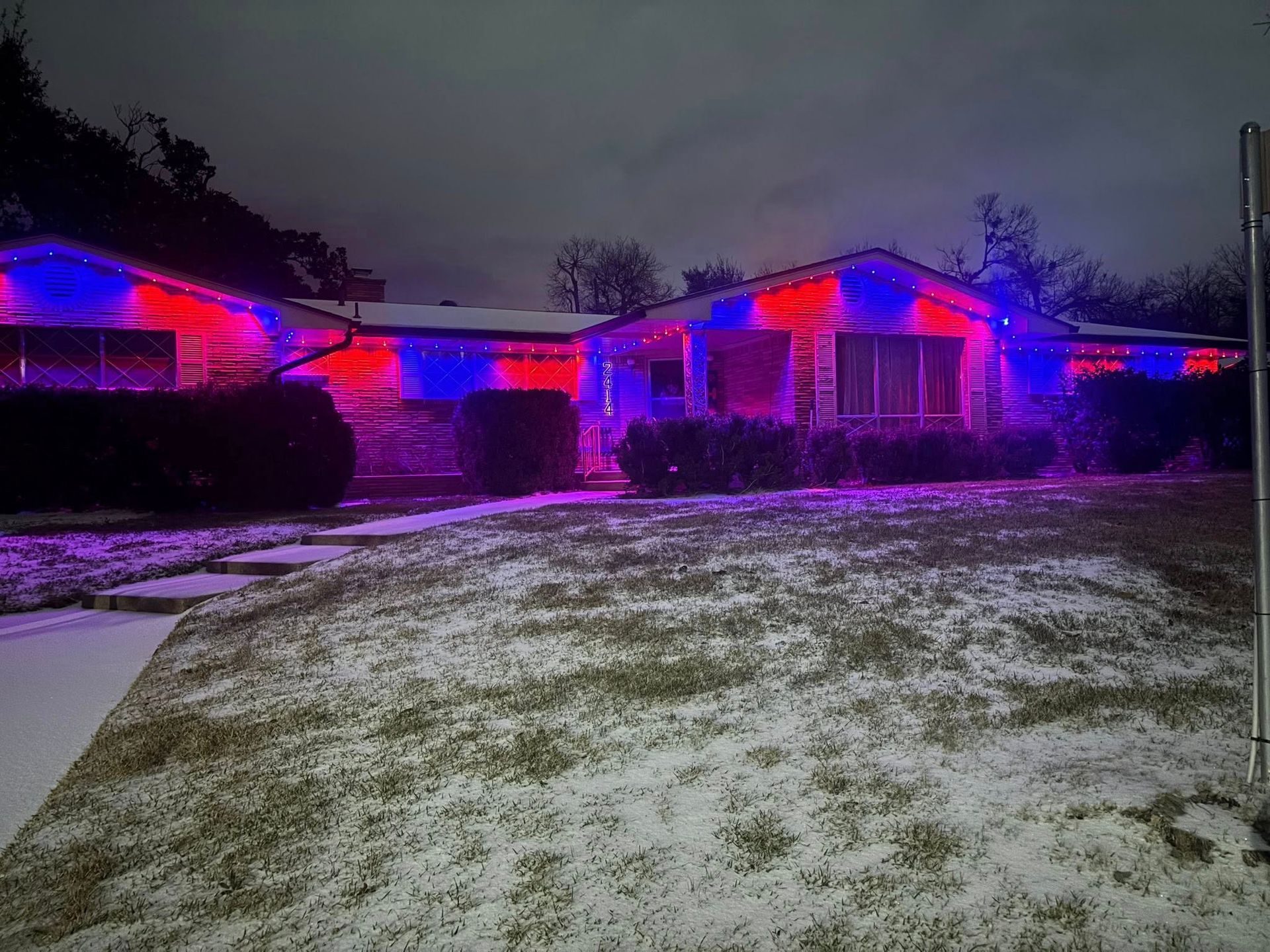 House lit with red and blue lights in a snowy yard at dusk
