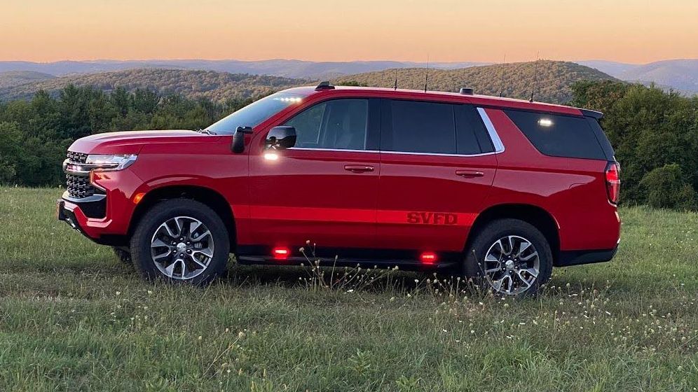 A red suv is parked in a grassy field with mountains in the background.