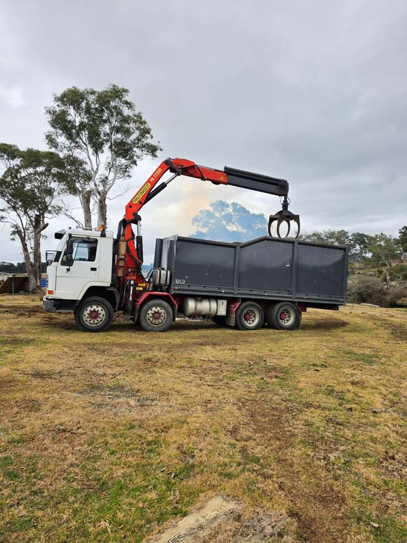 Dump truck loaded with scrap metal driving on a road beside trees at sunset