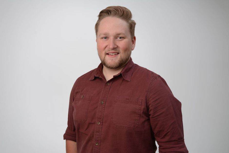 A man in a red shirt is standing in front of a white background.