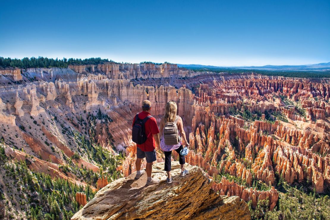 A man and a woman are standing on top of a rock overlooking a canyon.