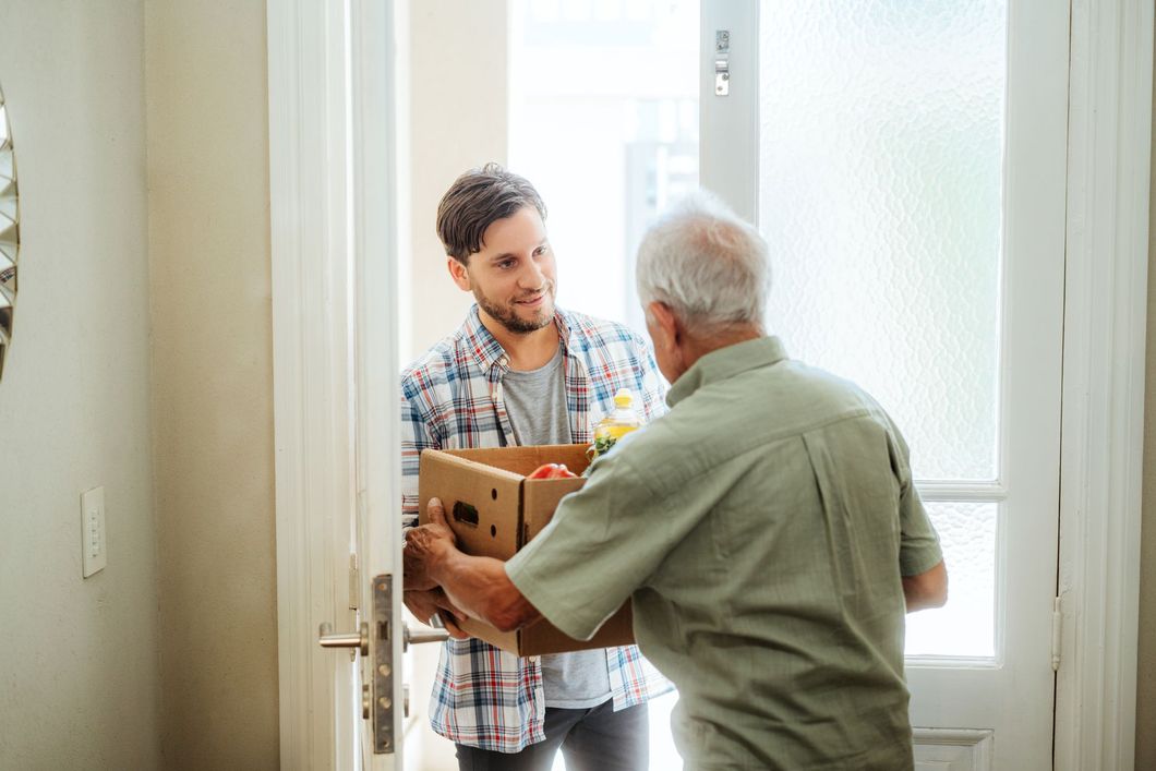 A man is giving a box of food to an older man.