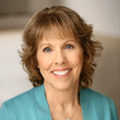 A woman in a blue jacket and necklace is smiling for the camera.
