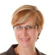A woman wearing glasses and a necklace smiles for the camera