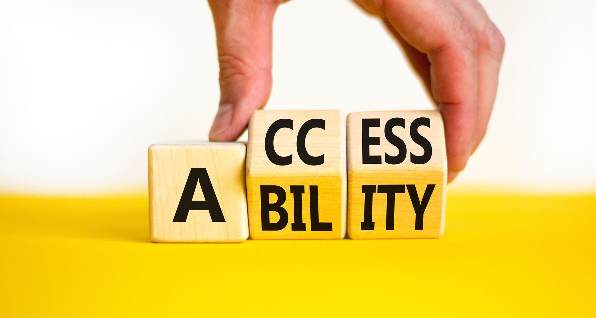 A person is holding wooden blocks with the words access ability written on them.