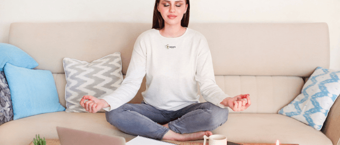 A person sitting cross-legged on the sofa, eyes closed, meditating with a peaceful expression.