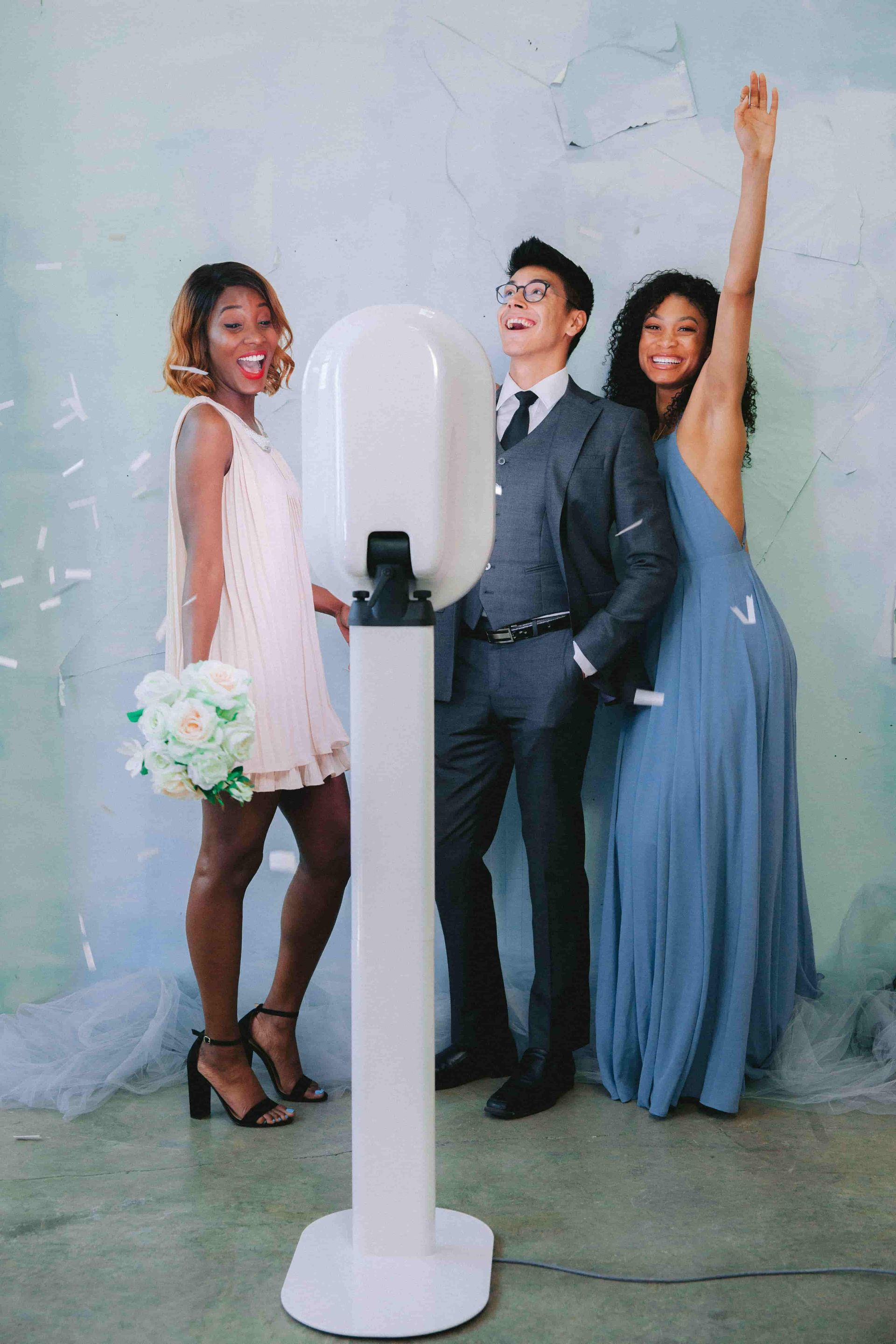 One man and two women all happy posing in front of a digital photo booth at a wedding
