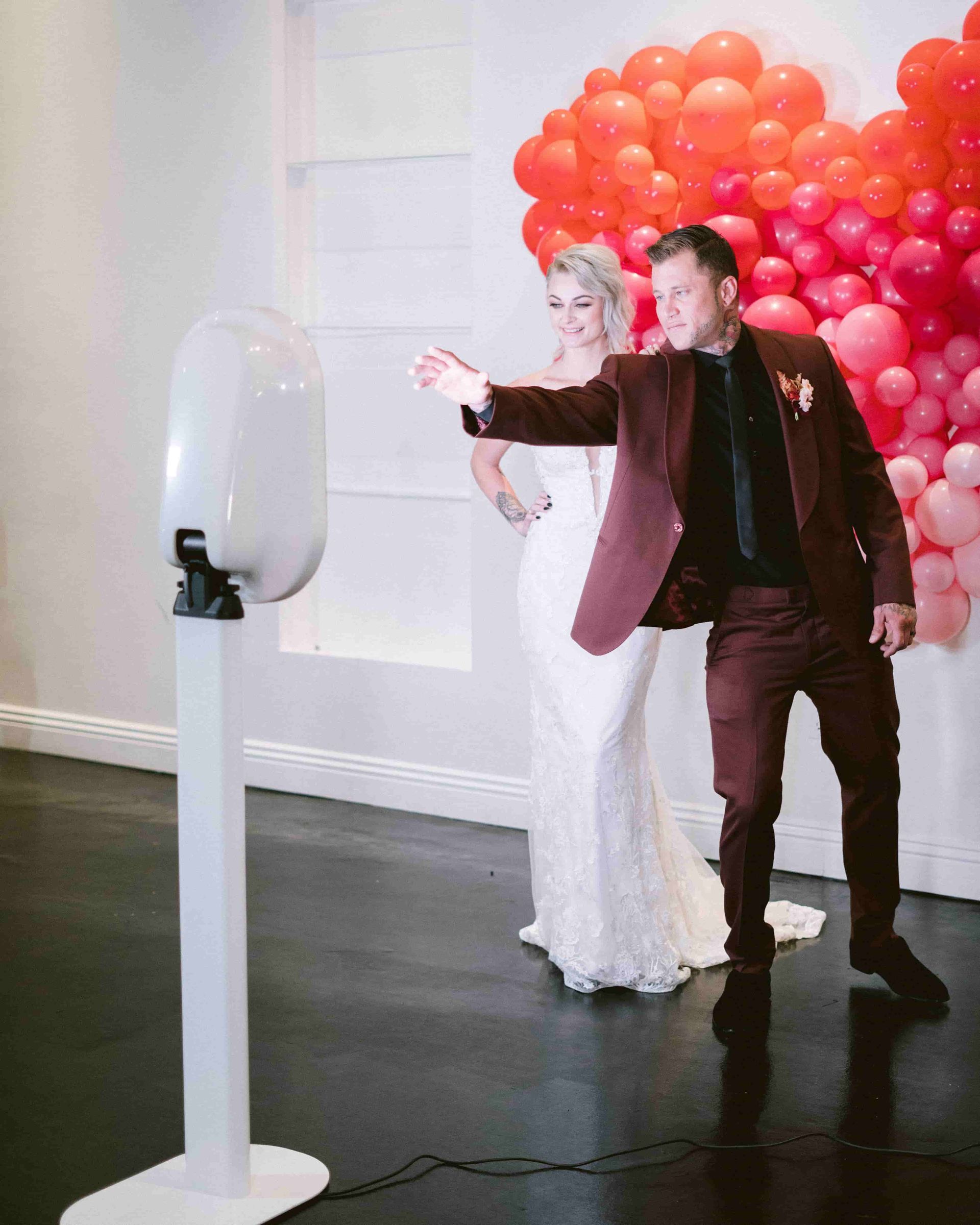 Couple holding hands in front of a digital photo booth and posing in front of a heart shaped backdrop