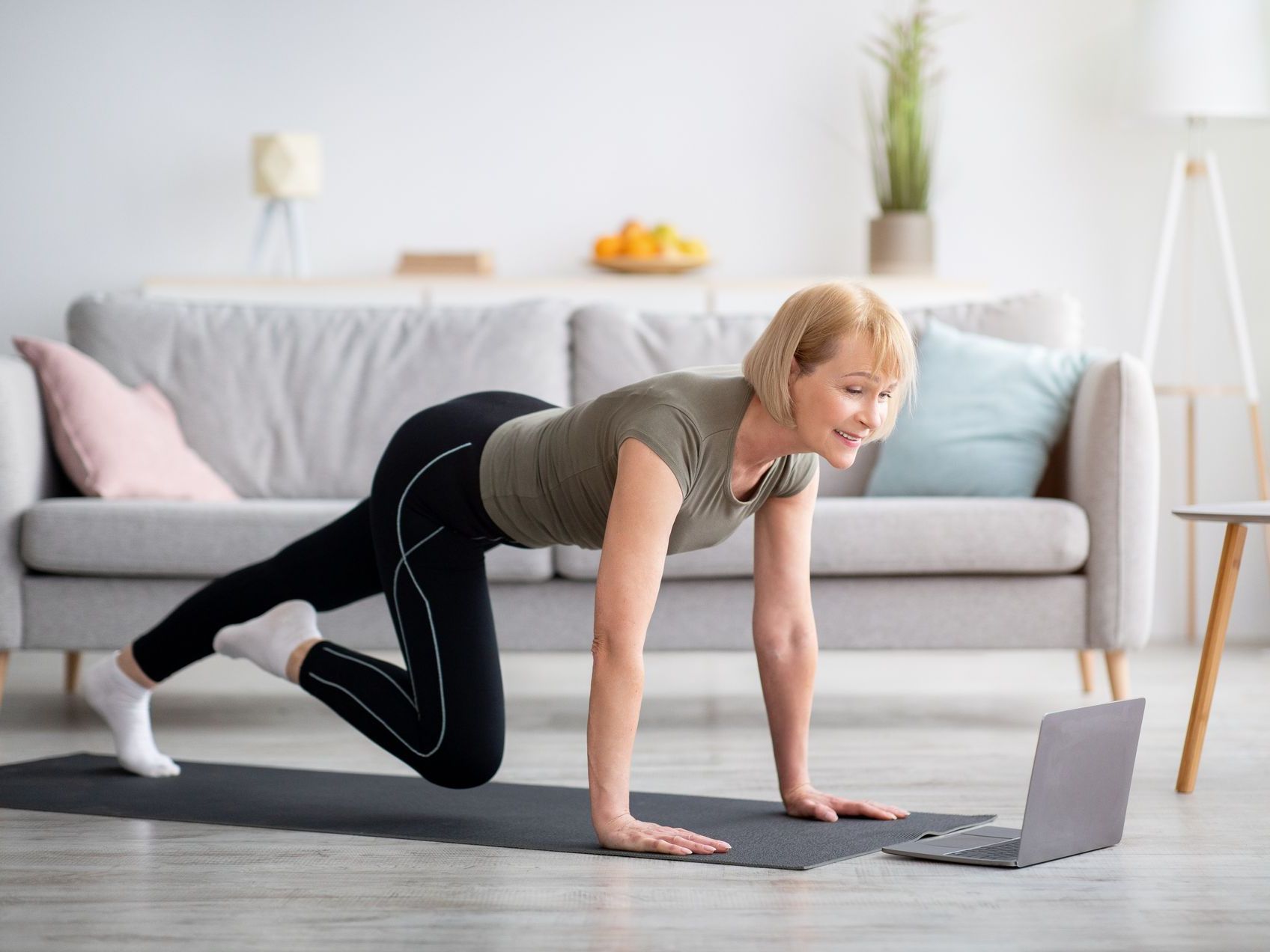 A woman is flexing her muscles while holding a yoga mat and a water bottle.