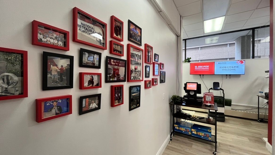Interior of the ZBS Minnesota office featuring a wall with a collage of framed pictures showcasing ZBS highlight moments. In the foreground, a table displays a ZBS point-of-sale system, highlighting the company's branding and workspace environment.