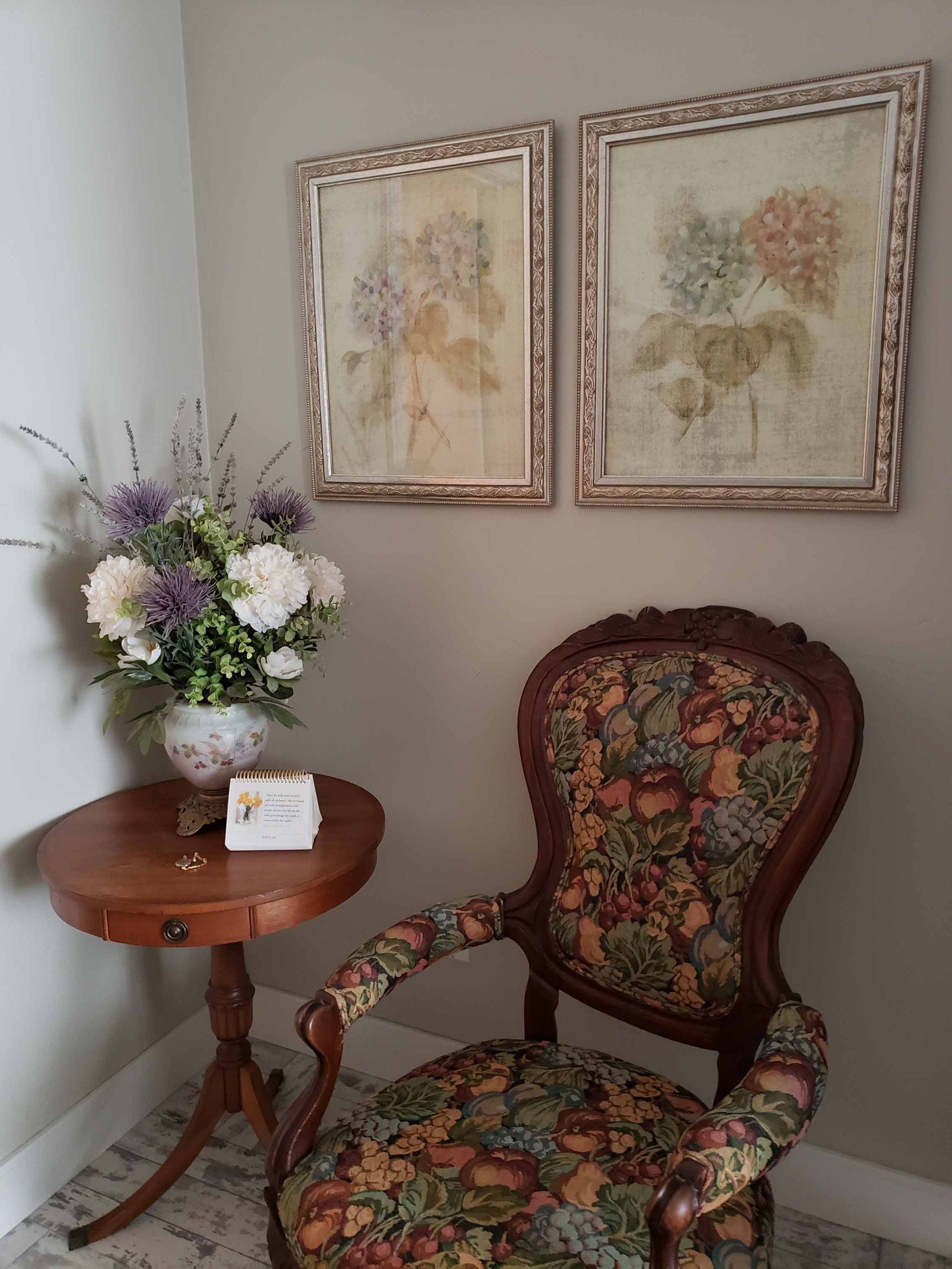 A chair sits next to a table with a vase of flowers on it