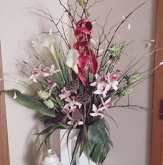 A vase filled with flowers and leaves is hanging on a wall