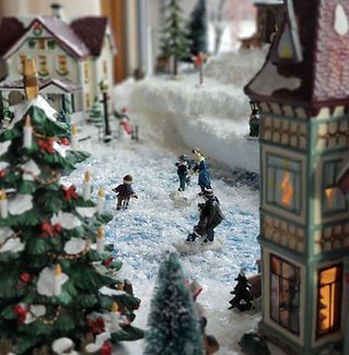 A miniature christmas village with a christmas tree and people playing in the snow.