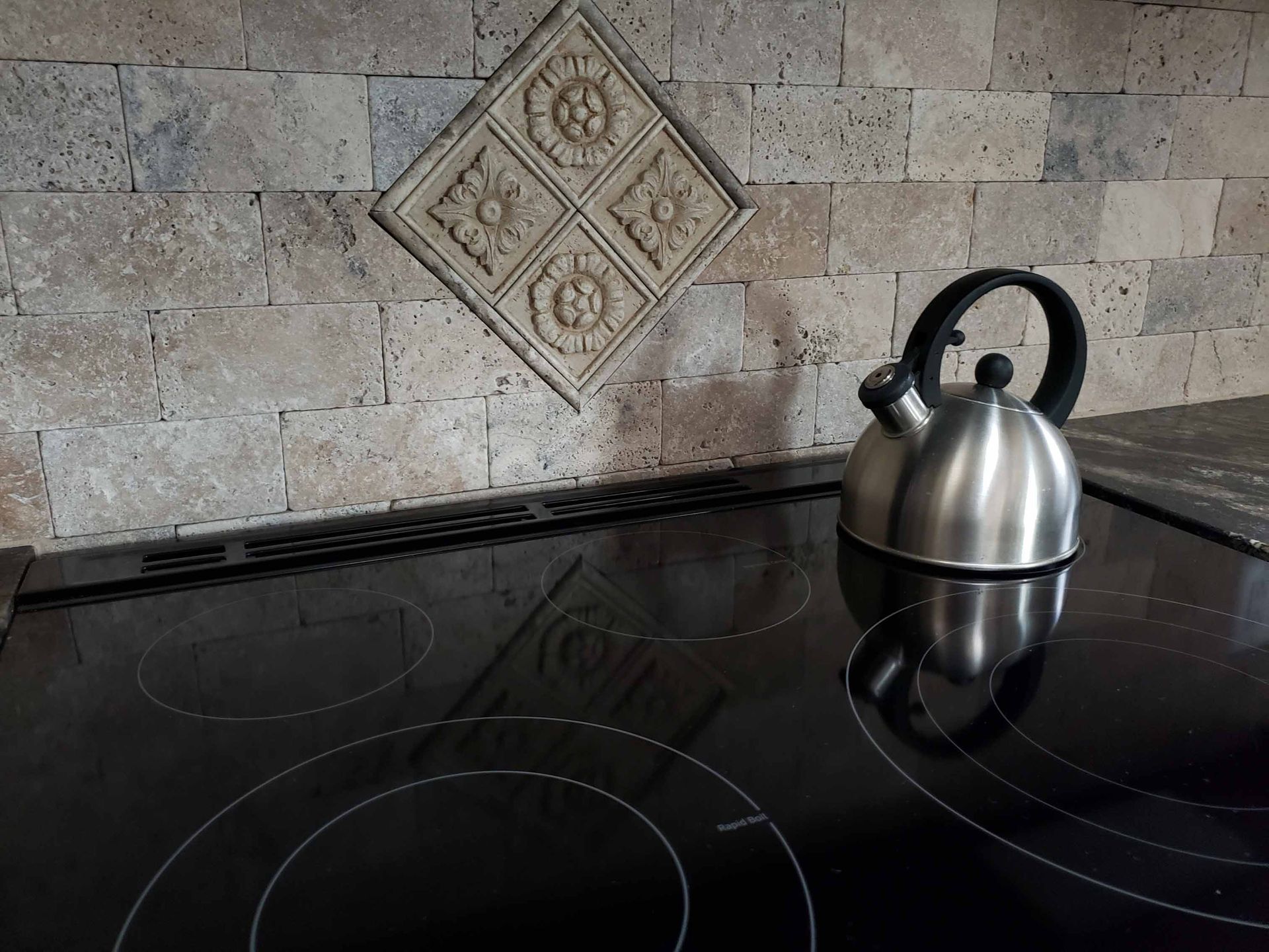 A stainless steel tea kettle is sitting on a black stove top