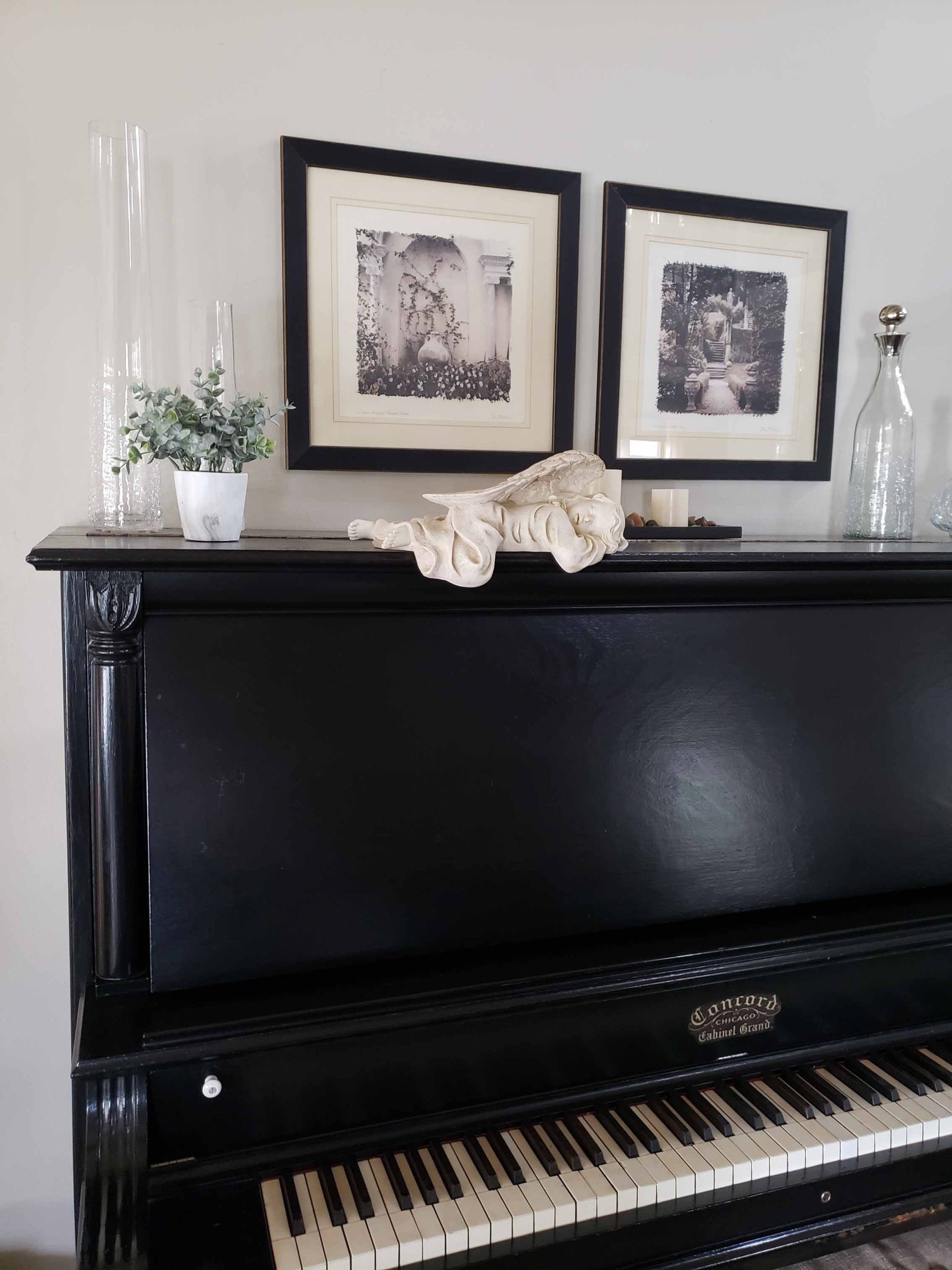 A black piano is sitting in a living room with pictures on the wall above it