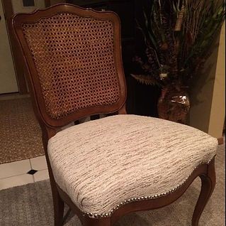 A chair with a cane back and a white cushion is sitting in a room next to a vase of flowers.