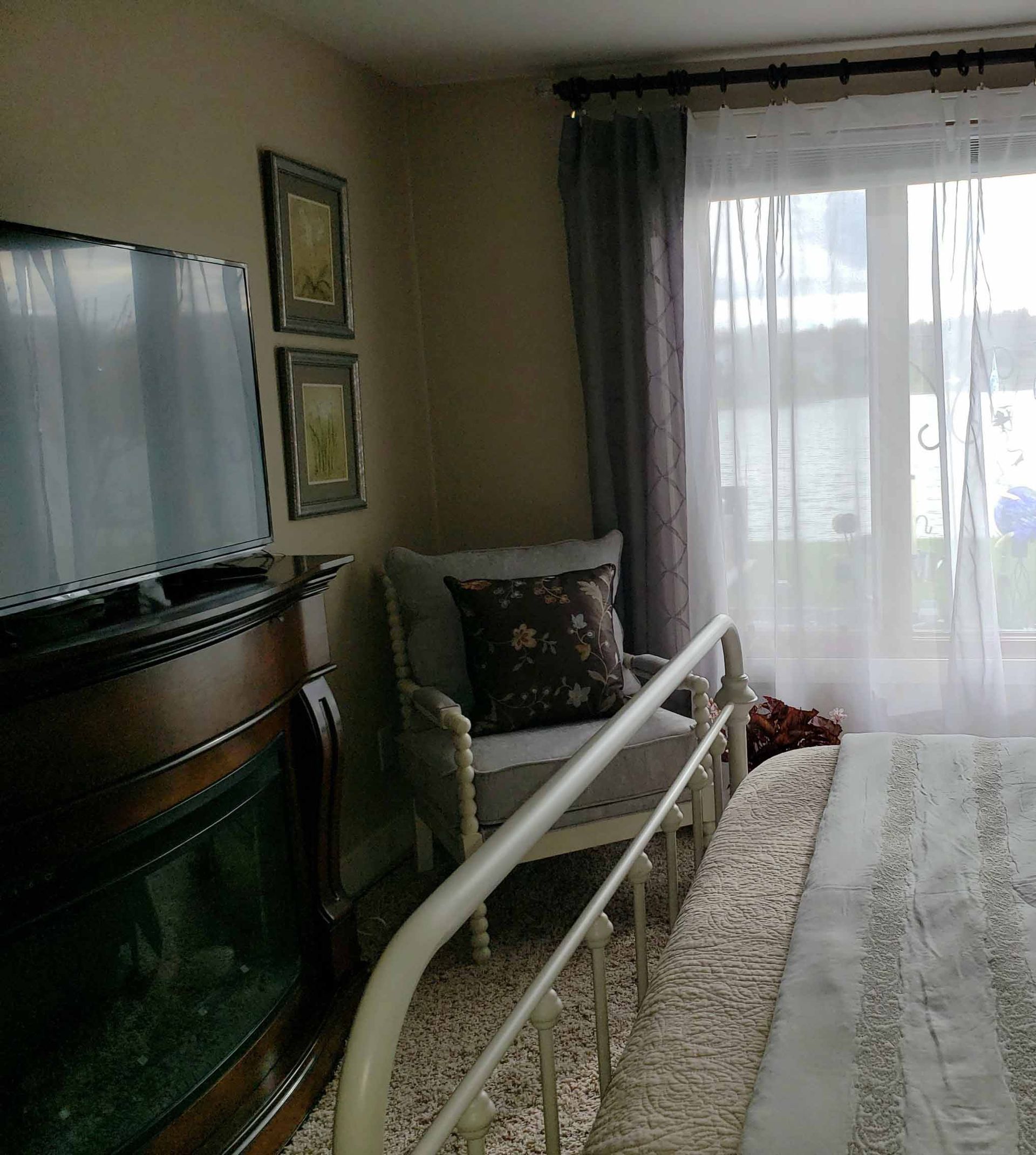A bedroom with a bed , chair , television and fireplace.