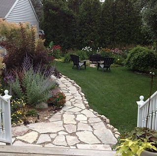 A stone walkway leads to a lawn with chairs and a table
