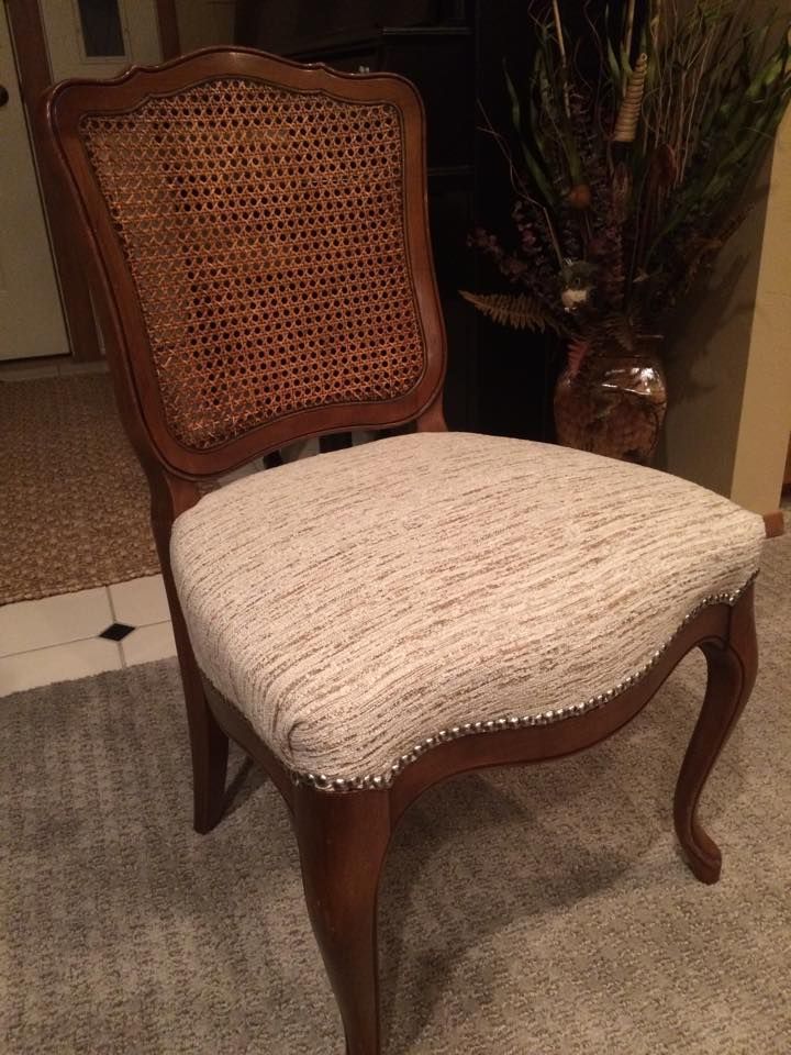 A chair with a cane back is sitting on a carpet next to a vase of flowers.