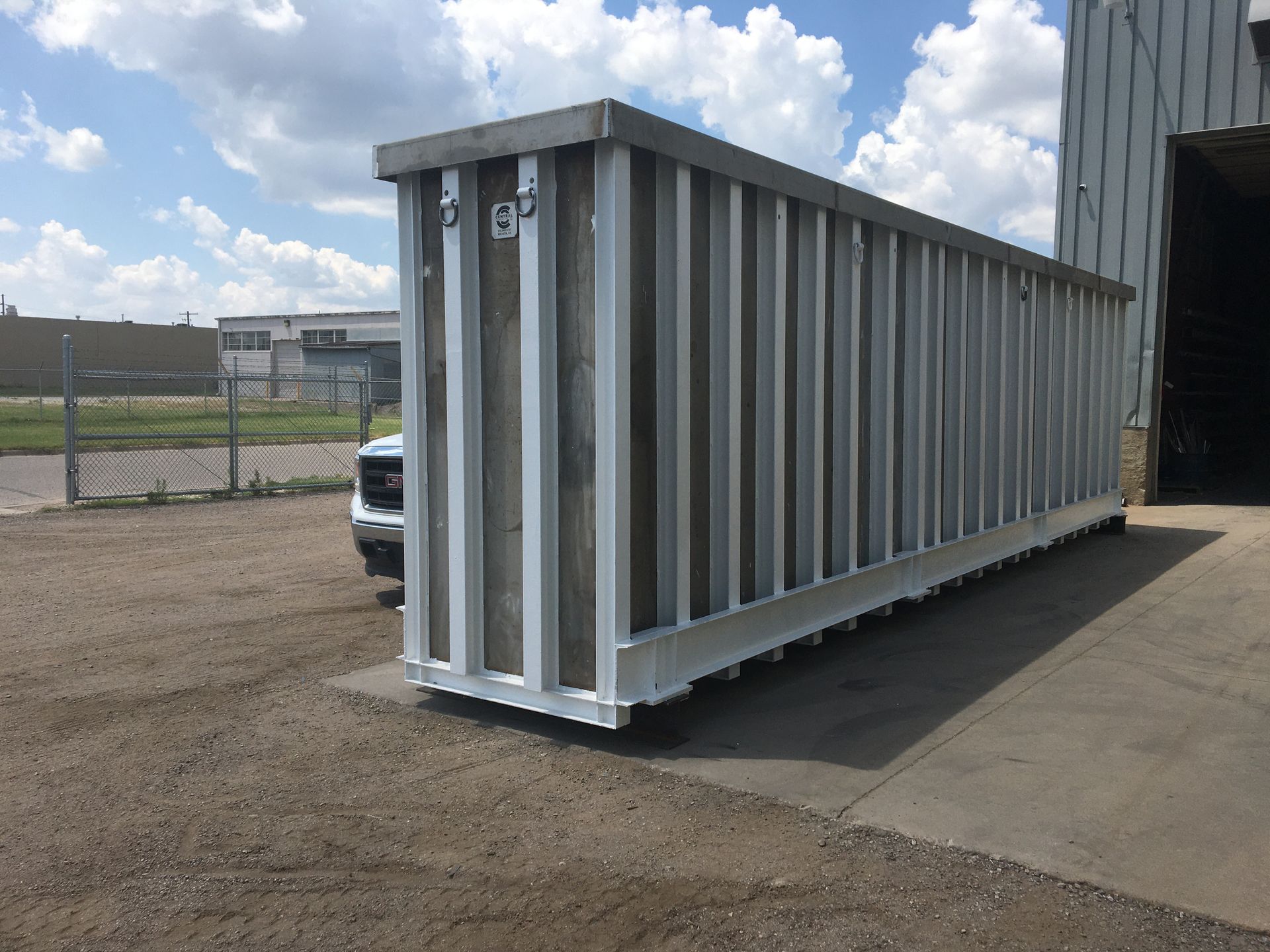 A large white container is sitting in a parking lot in front of a building.