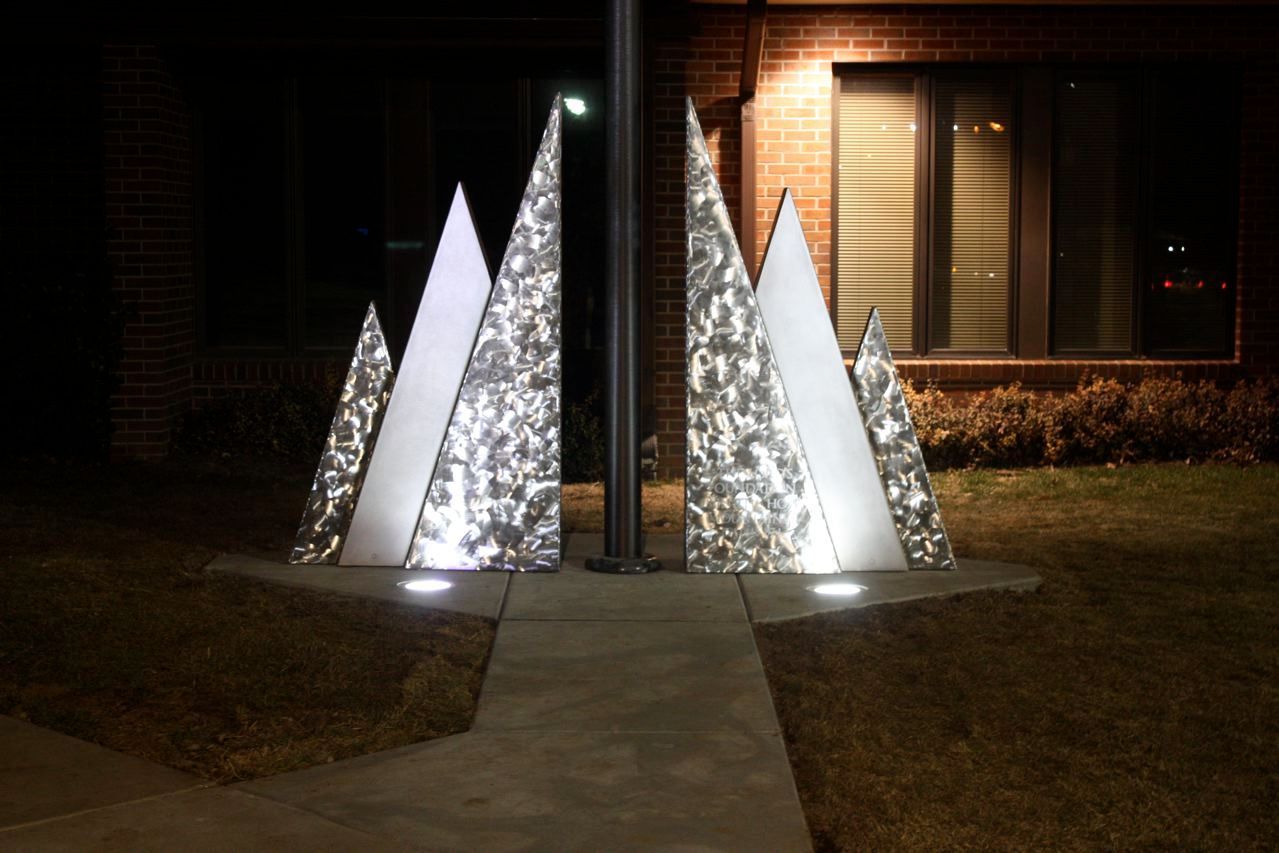 Three christmas trees are lit up in front of a house at night.