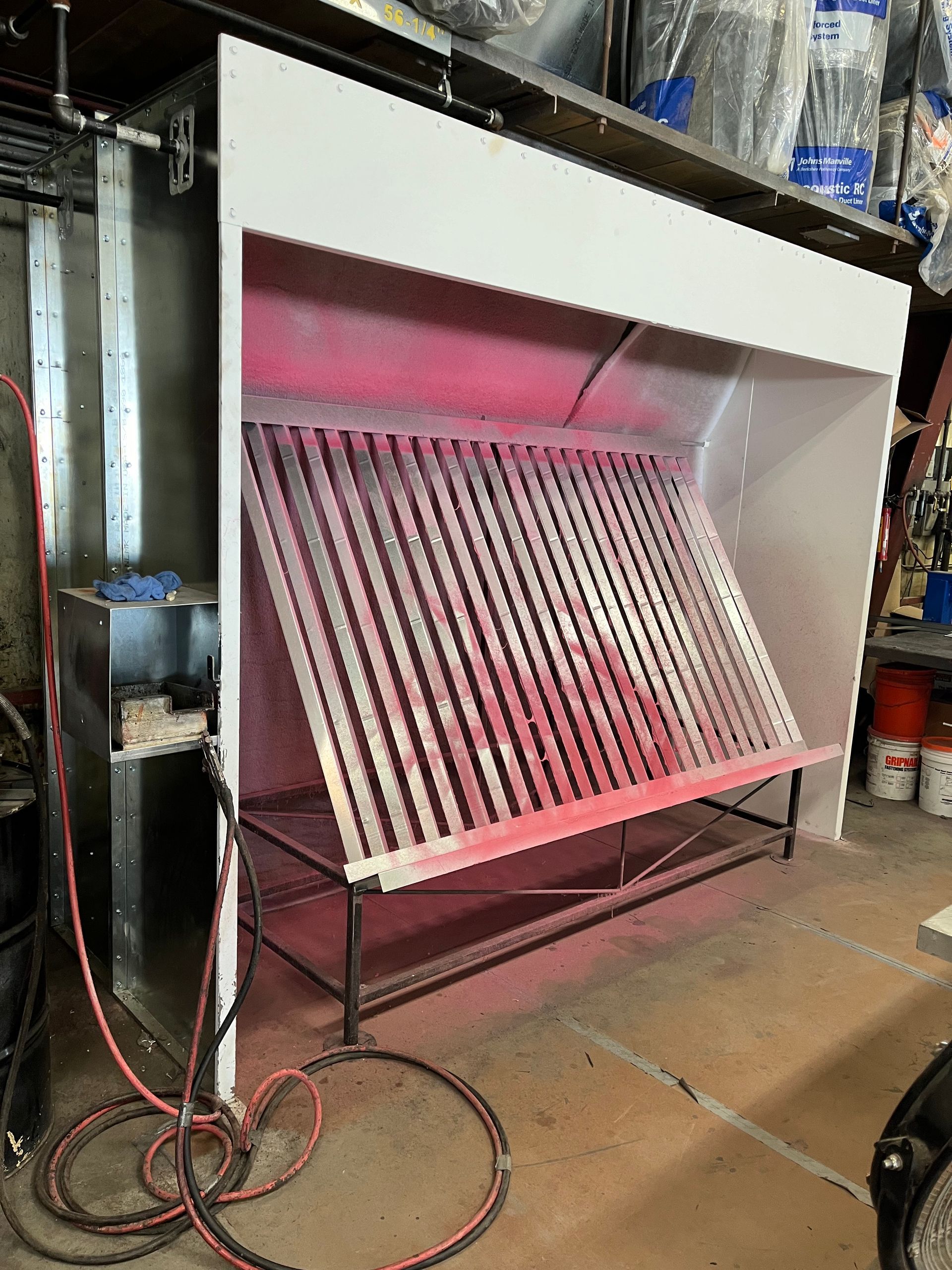 A spray booth is sitting in a garage with red paint coming out of it.