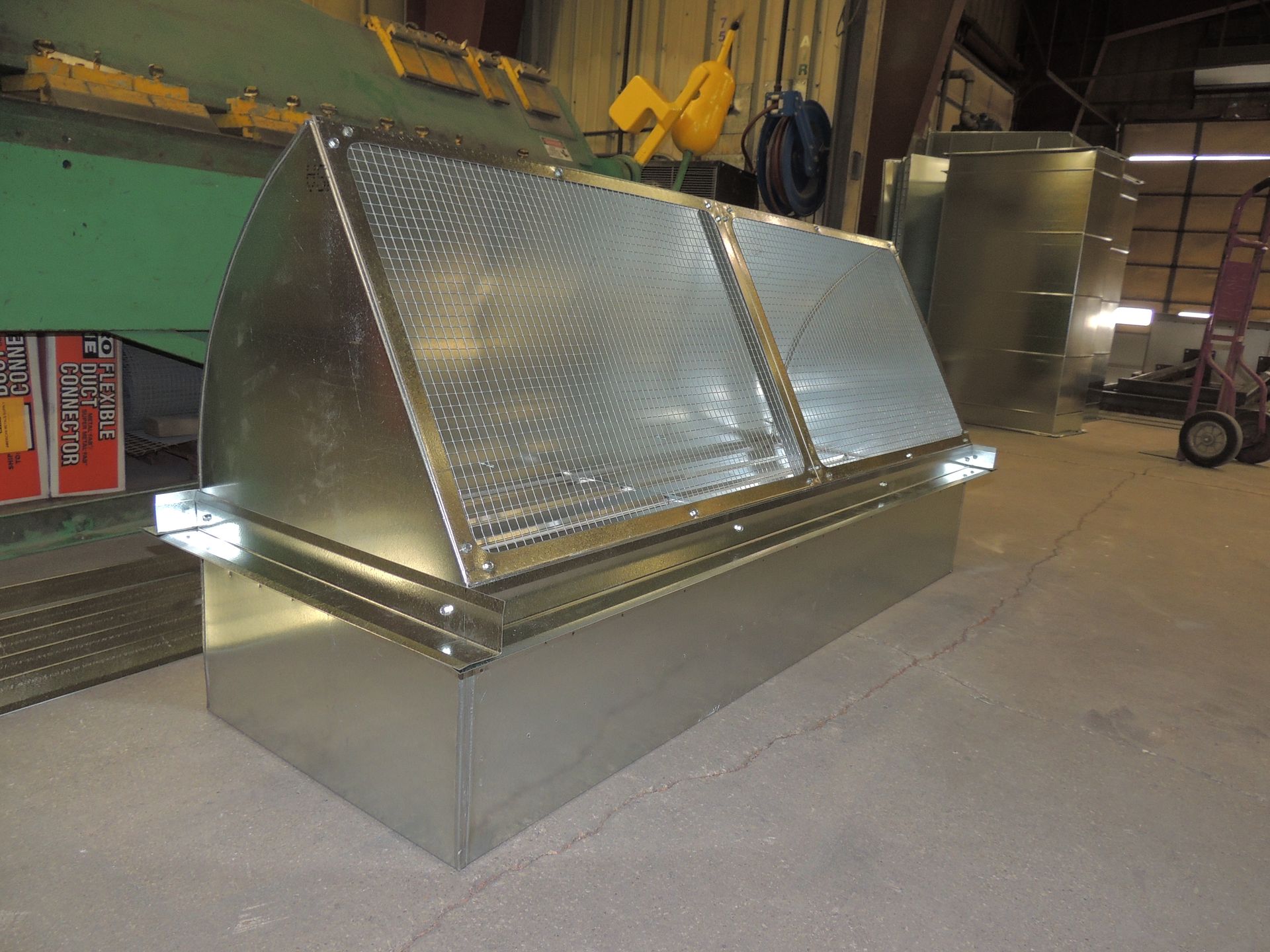 A large metal box for commerical HVAC is sitting on the floor in a factory.