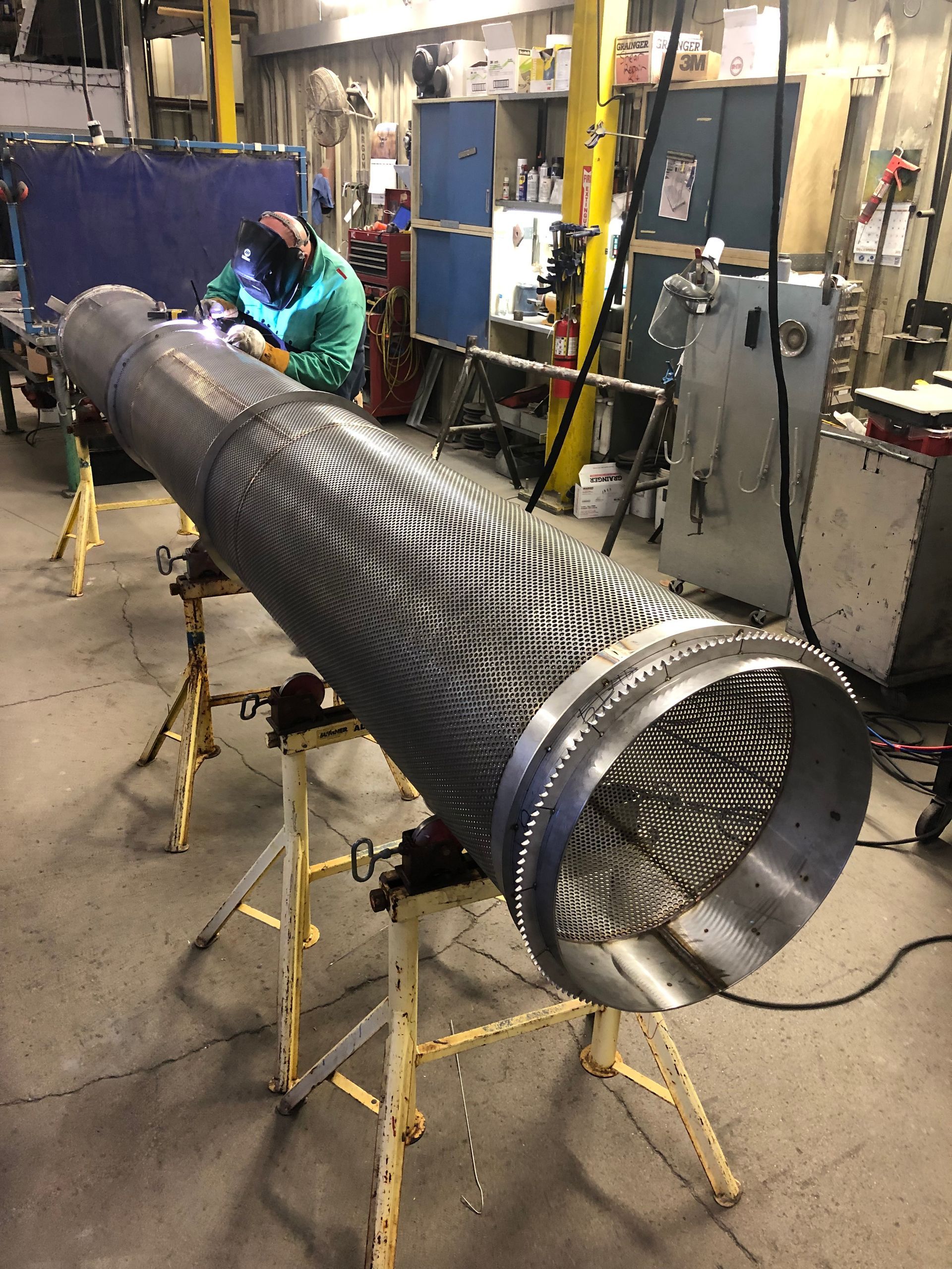 A man is welding a large metal pipe in a factory.
