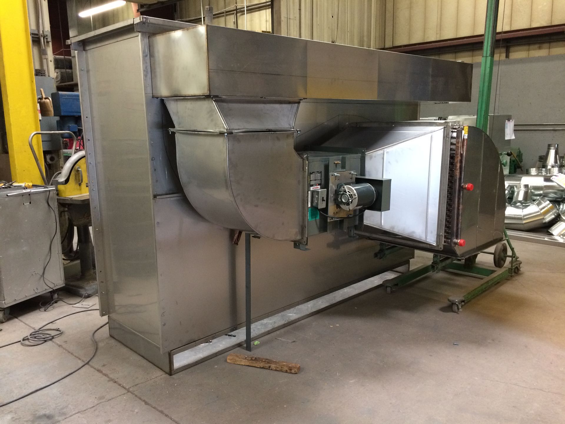A large stainless steel machine is sitting on the floor in a factory.