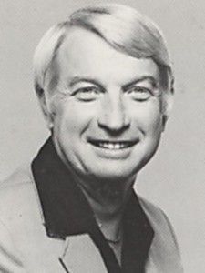 A man in a suit is smiling in a black and white photo.