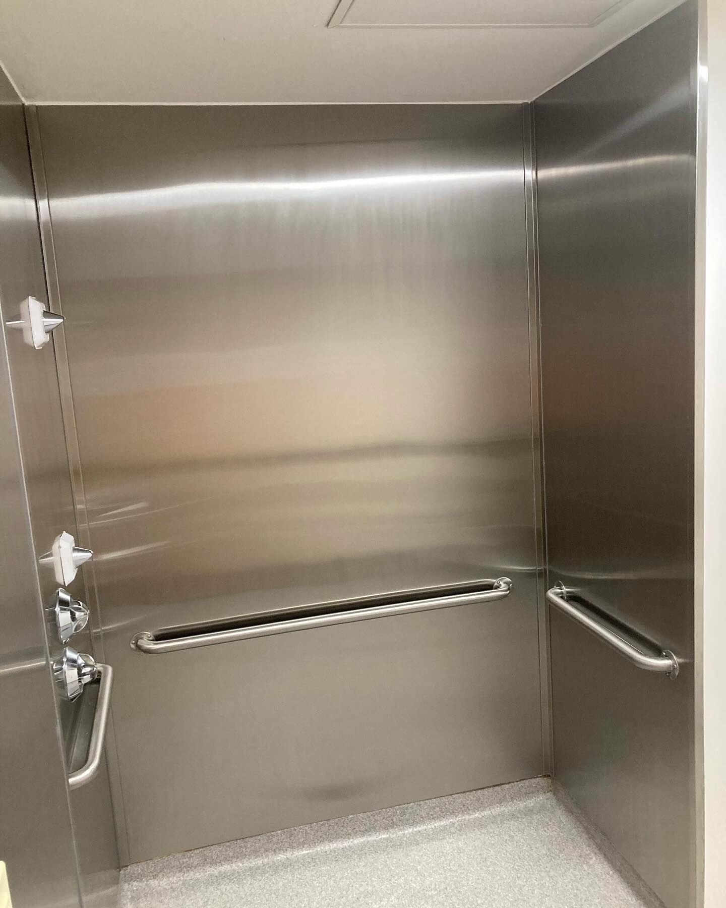 A bathroom with stainless steel walls and handrails.