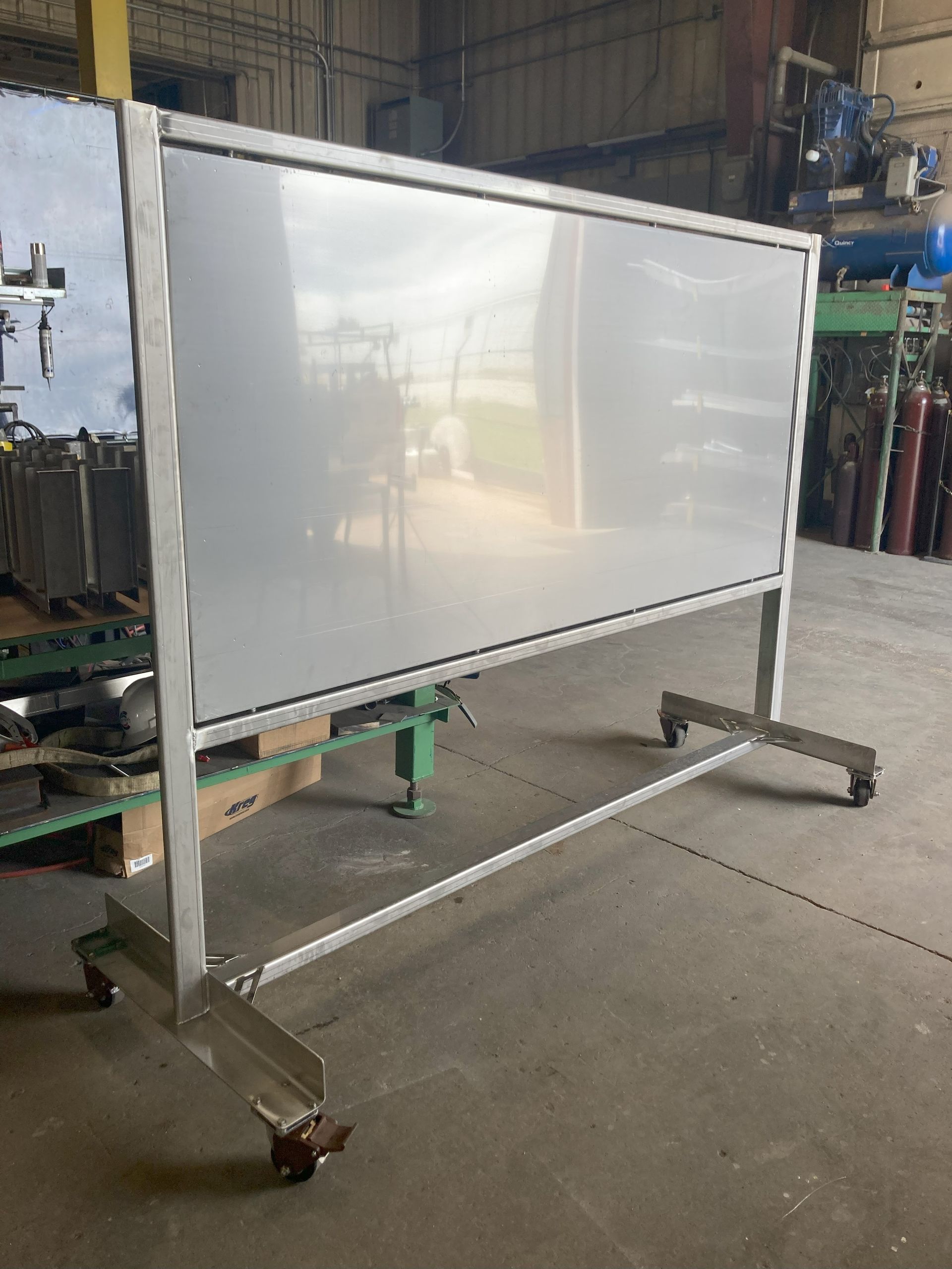A large whiteboard on wheels is sitting in a warehouse.