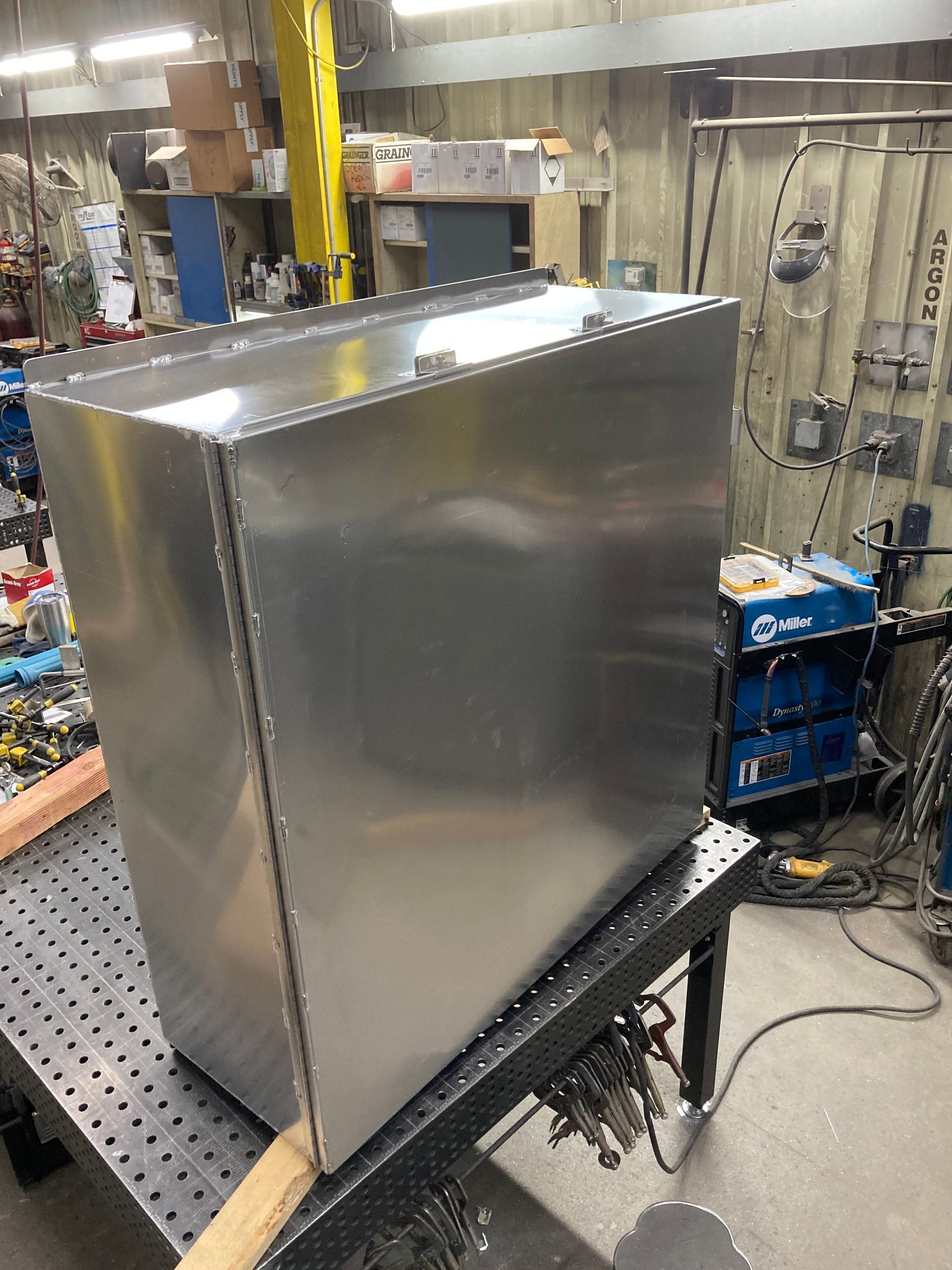 A large stainless steel box is sitting on top of a welding table.