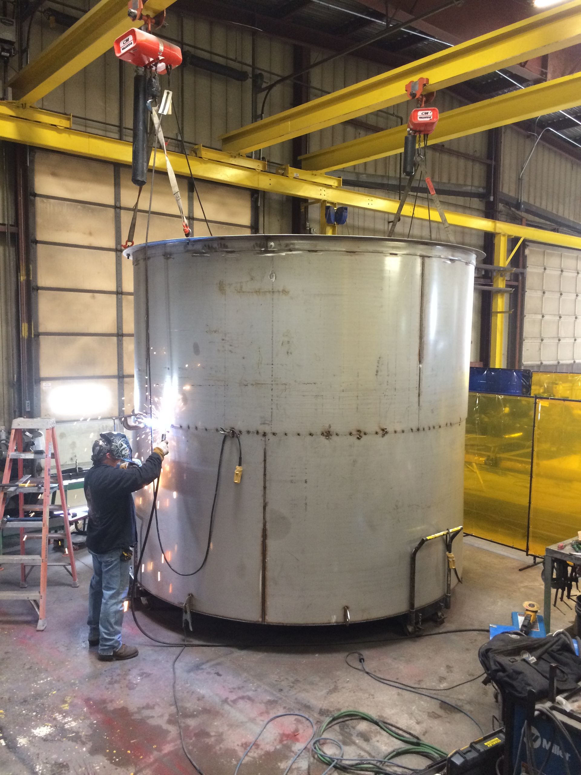 A man is welding a large metal object in a factory