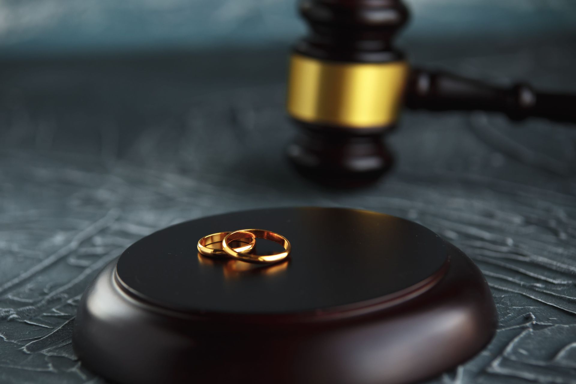 Wedding rings on a black auction gavel base, with a blurred gavel in the background.