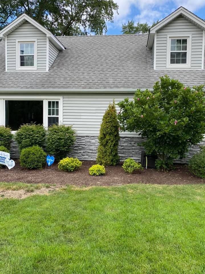 Suburban house with white siding, gray roof, green lawn, and landscaped front shrubs