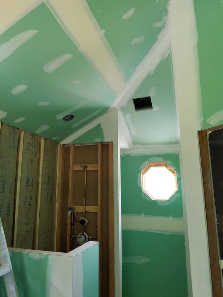 Partially finished bathroom with green drywall, exposed studs, and a small octagonal window.