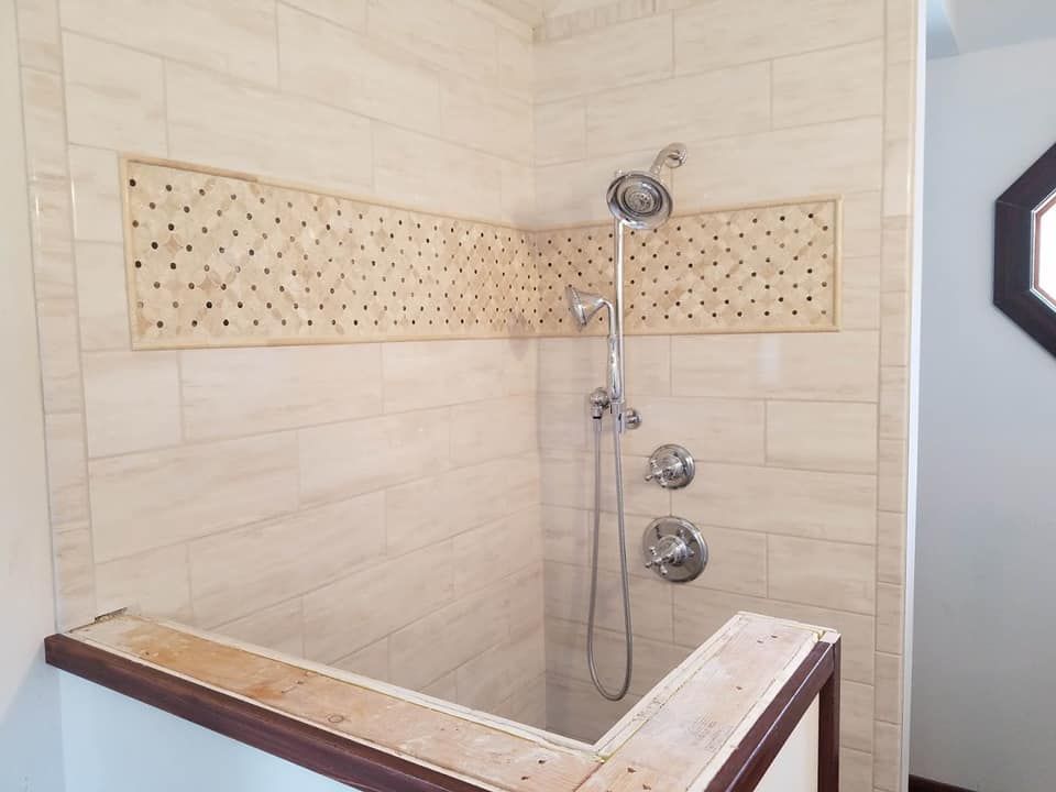 Accessible tiled shower with bench, grab bar, handheld showerhead, and control fixtures.