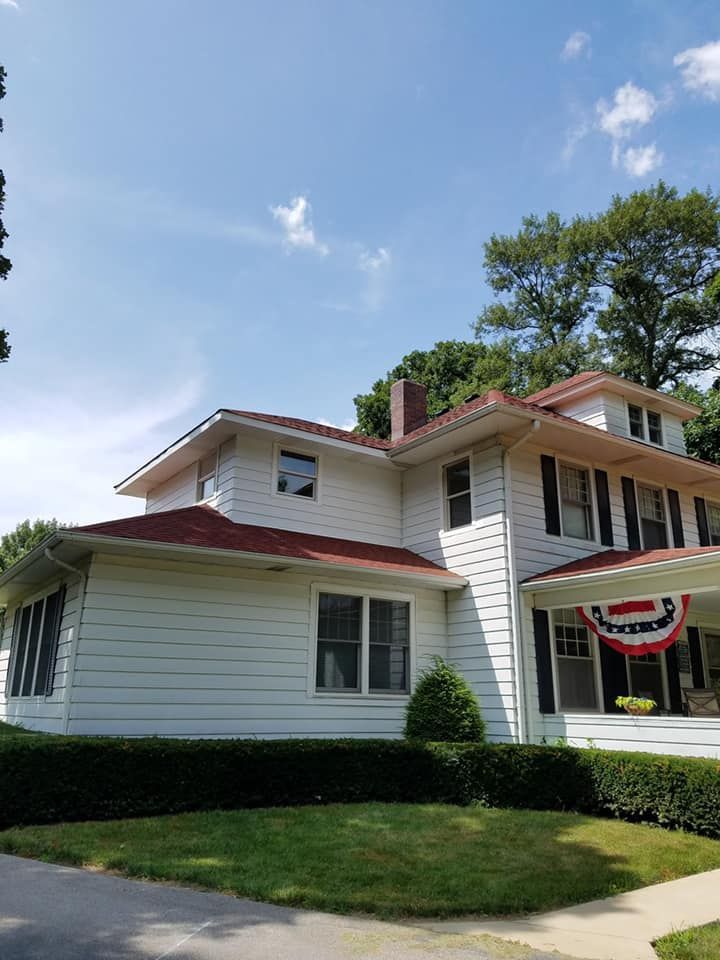 White house with red roof trim, striped porch awning, and manicured lawn on a sunny day.