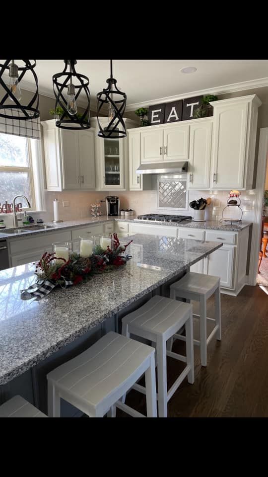 Bright white kitchen with granite island, stools, pendant lights, and decor on the counter.