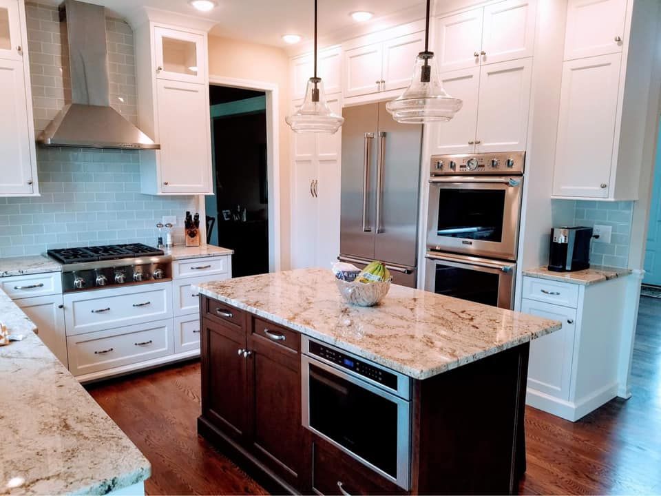 Bright kitchen with white cabinets, granite island, stainless steel appliances, and wood floors