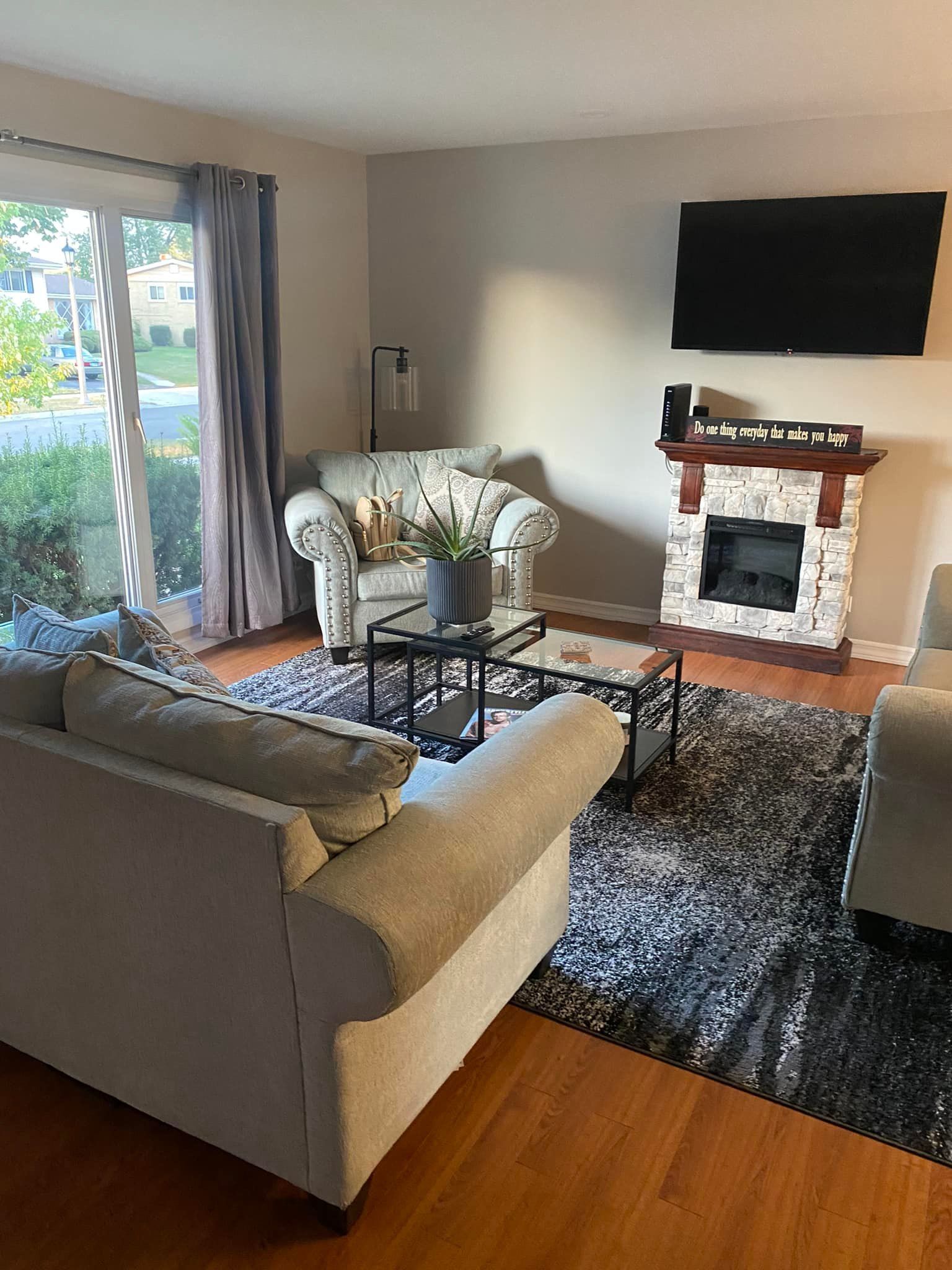 Cozy living room with gray sofa, glass coffee table, fireplace, wall-mounted TV, and sliding glass doors.