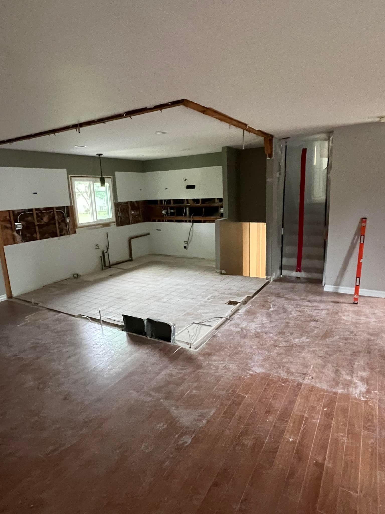 Partially renovated kitchen with exposed flooring, white cabinets, and a doorway to another room