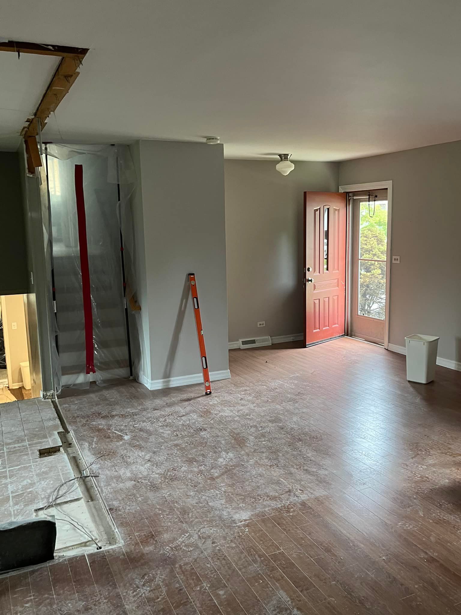 Empty living room with wood floor, open front door, and ladders during renovation