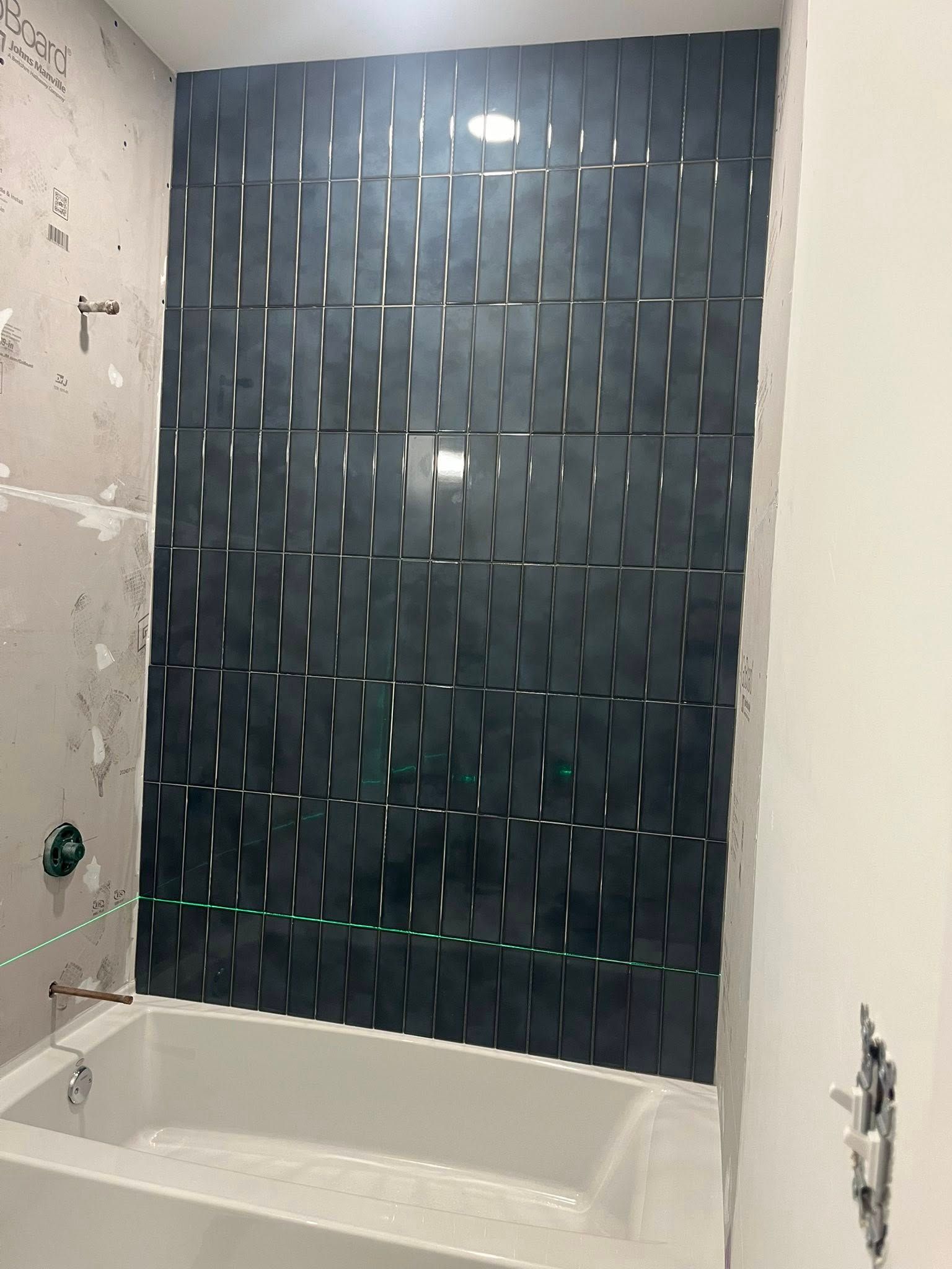 Bathroom tub with dark green tile accent wall and unfinished surrounding drywall.