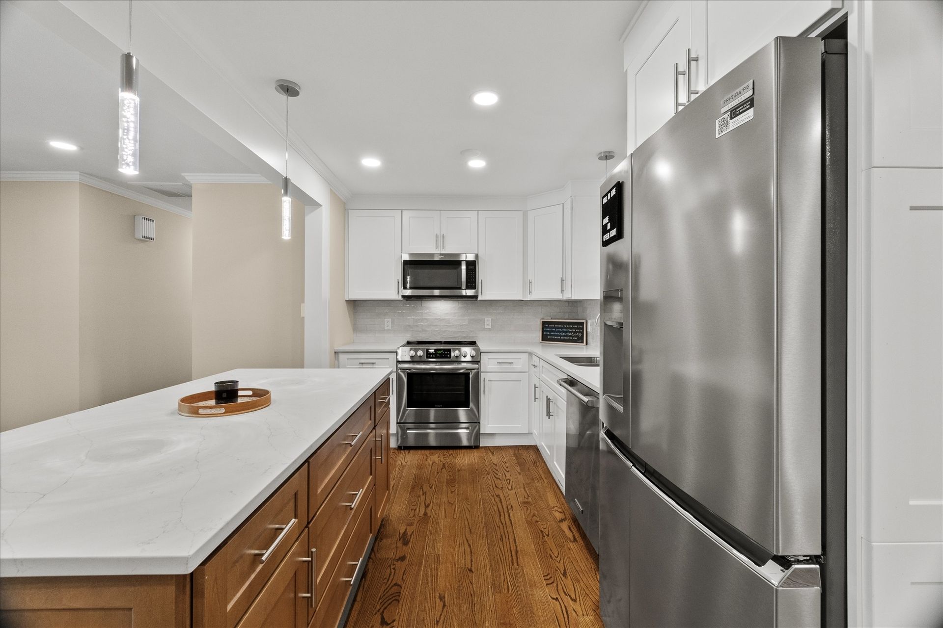 Modern white kitchen with stainless steel appliances, wood floor, and marble island countertop